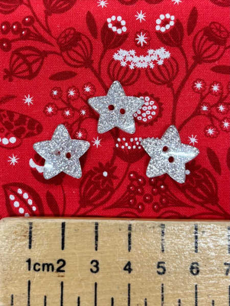 Silver glitter star button by Trimits, 18mm, shown against a festive red fabric background with ruler for scale.