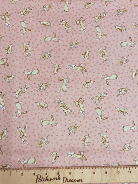 Clothworks UK Guess How Much I Love You pink quilting fabric with playful bunnies and tiny dandelion heads on a blush background.