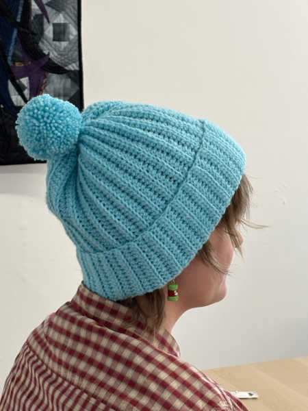 Person wearing a hand-crocheted light blue ribbed hat with a pom pom, made during the Crochet Pom Pom Hat Workshop at Patchwork Dreamer in Bodmin.