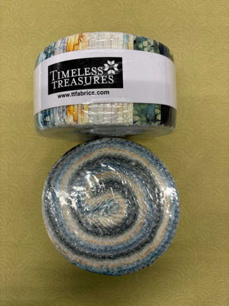Timeless Treasures UK Whisper jelly roll showing soft blue, grey, cream, and golden fabric strips rolled together with collection label.