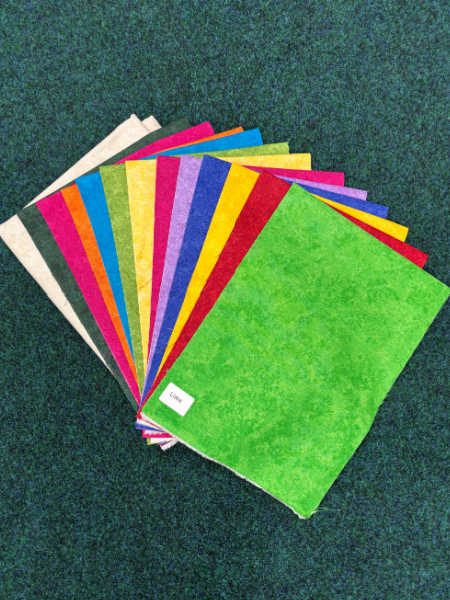 A fan of colourful fabric pieces in bright shades of green, yellow, red, pink, blue and cream from the Hector’s Year fabric-only quilt kit by Patchwork Dreamer.