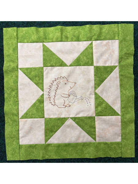 August block from Hector’s Year BOM showing a green and cream star block with an embroidered hedgehog watering the garden.