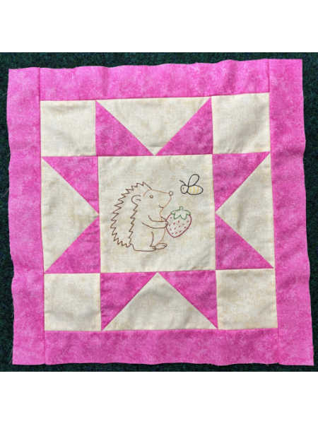 June block from Hector’s Year BOM showing a pink and cream star block with an embroidered hedgehog holding a strawberry and a bee.