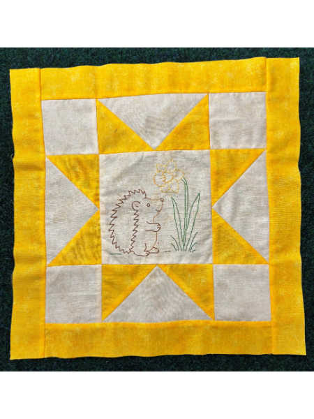 March block from Hector’s Year BOM featuring a yellow and cream star block with an embroidered hedgehog looking at a daffodil.