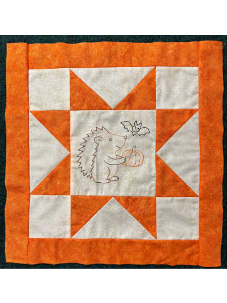 October block from Hector’s Year BOM showing an orange and cream star block with an embroidered hedgehog holding a pumpkin and a small bat.