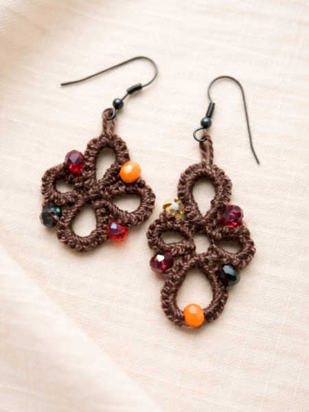 Brown tatted lace earrings with colourful beads, displayed on a soft cream linen background