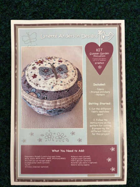 Summer Garden pincushion kit by Lynette Anderson Designs showing a round fabric pincushion with embroidered flowers in soft pastel colours, UK.