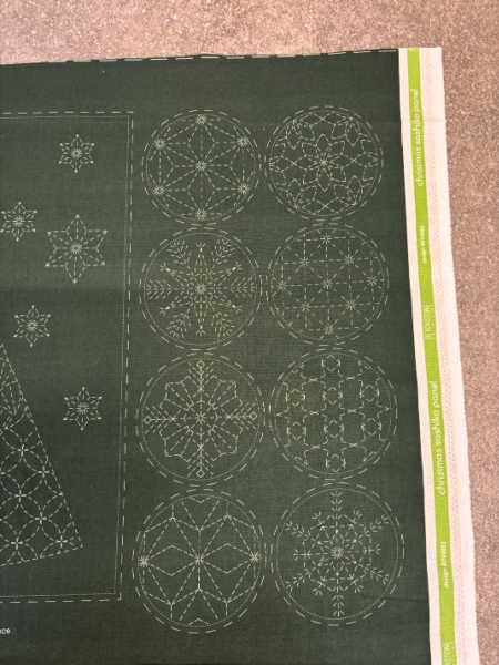 Christmas sashiko deer design with patterned trees and a circular snowflake background on dark green linen cotton fabric.